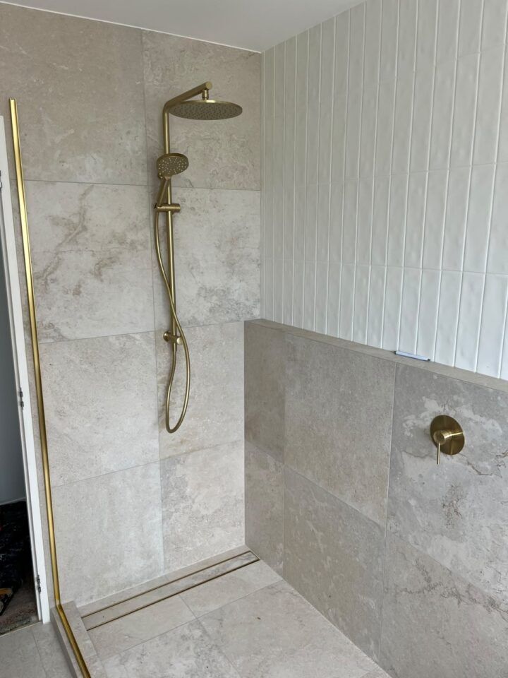 Finished shower with brushed brass tapware and a linear floor drain