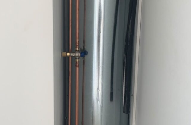 Hot water cylinder installed indoors with pipework and valves