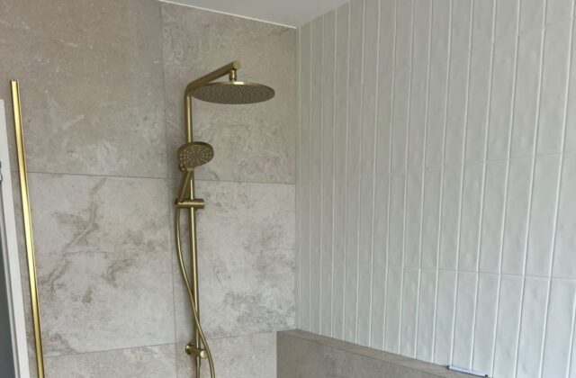 Brushed brass shower head and rail in a travertine shower